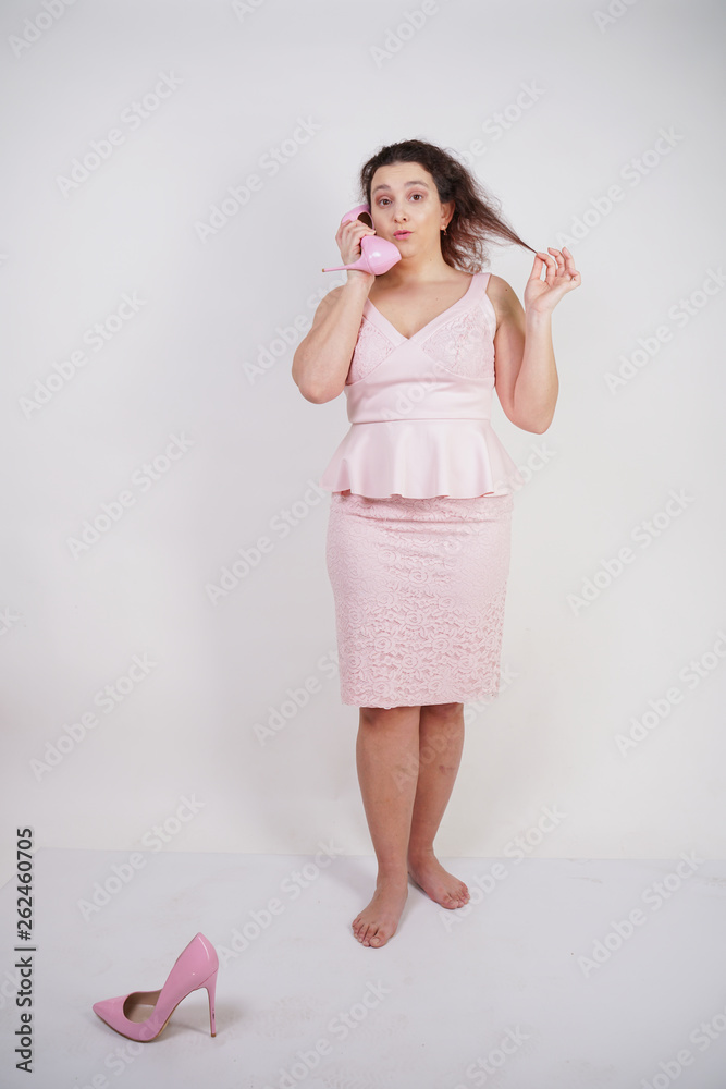 emotional plump woman in pink dress talking and gossips on the Shoe like on the phone on a white Studio background emotional plump woman in pink dress talking and gossips on the Shoe like on the phone on a white Studio background