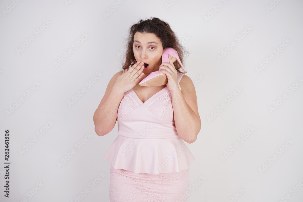 emotional plump woman in pink dress talking and gossips on the Shoe like on the phone on a white Studio background emotional plump woman in pink dress talking and gossips on the Shoe like on the phone on a white Studio background