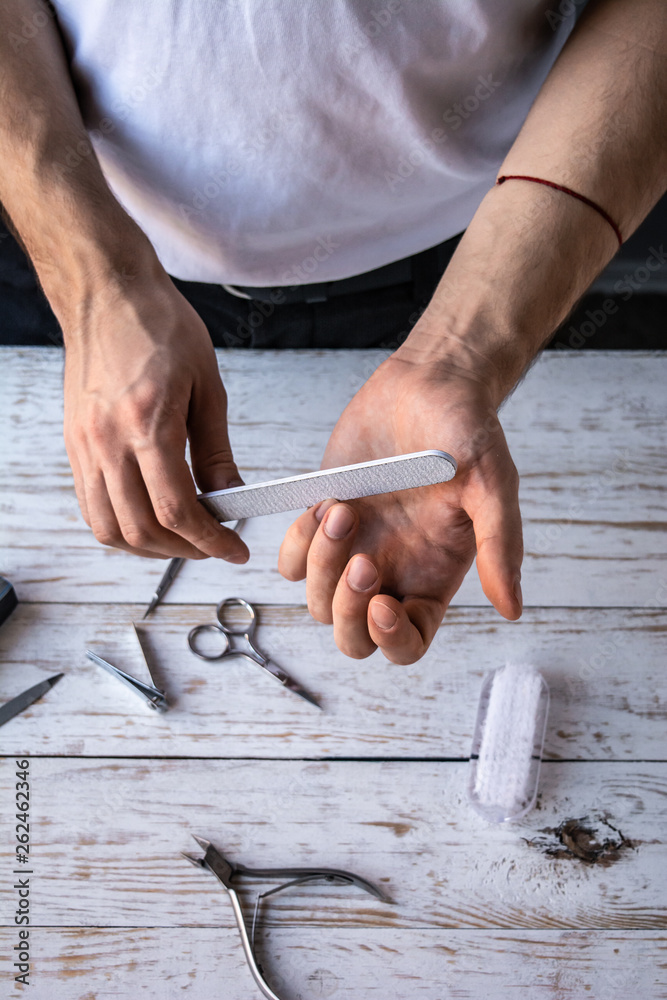 Close-up male hands. Man making manicure with a nail file. White wooden table. Close-up male hands. Man making manicure with a nail file. White wooden table.