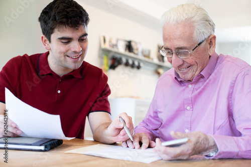 Young Man Helping Senior Neighbor With Paperwork At Home