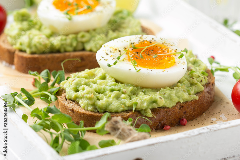 Toast with avocado puree and soft-boiled egg on white tray, liquid yolk, delicious breakfast, light sandwich. Healthy food