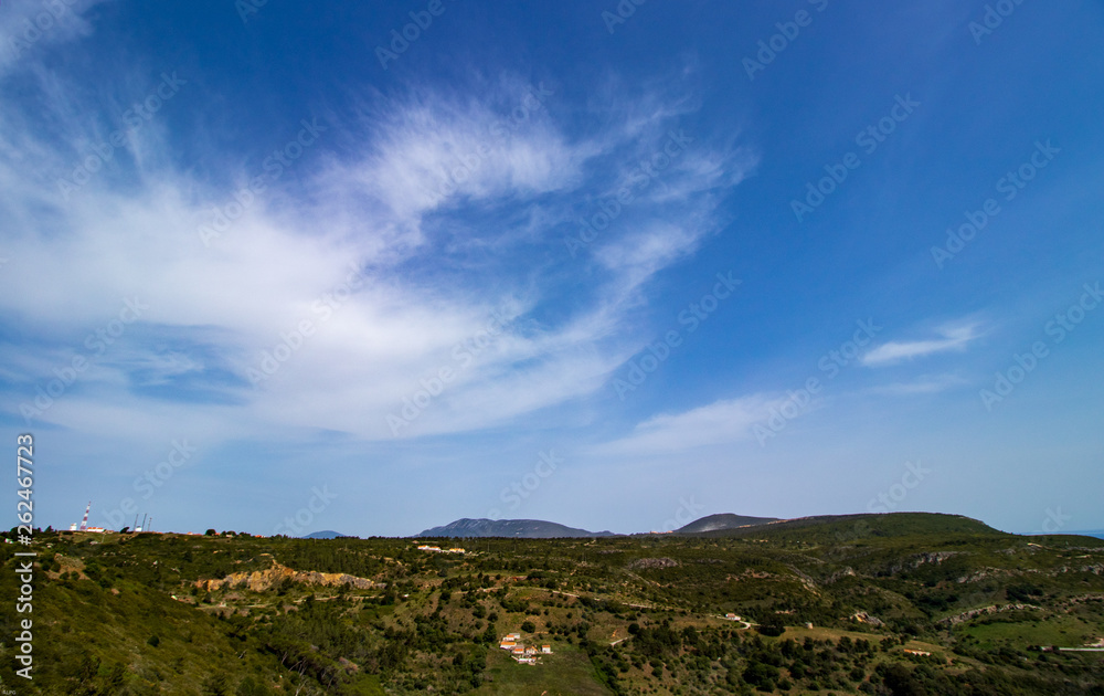 blue sky with soft white clouds and green fields below