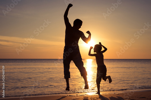 Father and son playing on the beach at the sunset time.