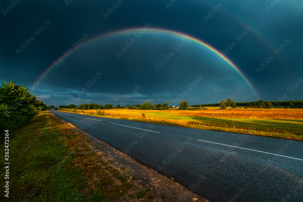 Double rainbow over the highway in darkly blue sky after a rain