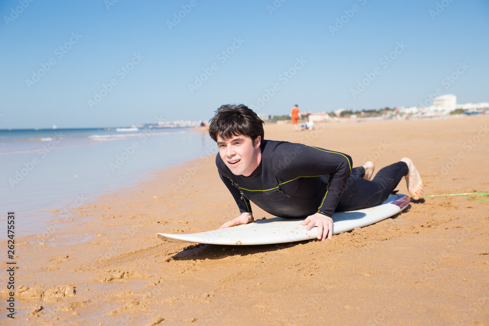 Excited young man learning to stand up on surfboard on beach