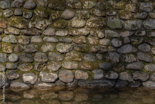 Old stone wall covered with moss, reflected in the water - a beautiful vintage background
