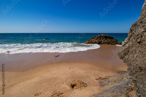 Sand, rocks, white foam and blue sky on the beach