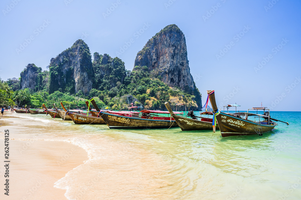 Fototapeta premium Longtail boats moored near the Railay Beach, Krabi / Thailand. Mountains with trees on the background. Clean blue sky