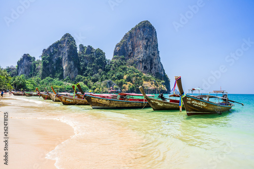 Longtail boats moored near the Railay Beach, Krabi / Thailand. Mountains with trees on the background. Clean blue sky © valeragf