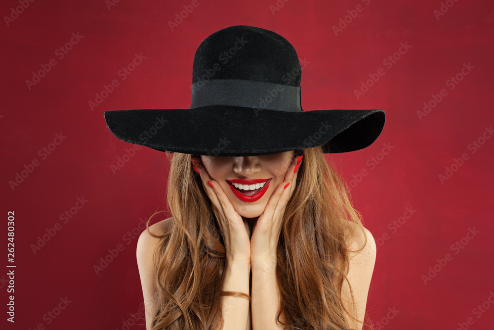 Happy model woman with red lips makeup and manicure on red background. Pretty surprised model in black hat portrait Happy model woman with red lips makeup and manicure on red background. Pretty surprised model in black hat portrait