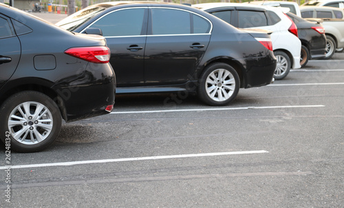 Closeup of rear, back side of black car and other cars parking in outdoor parking lot in twilight evening. 