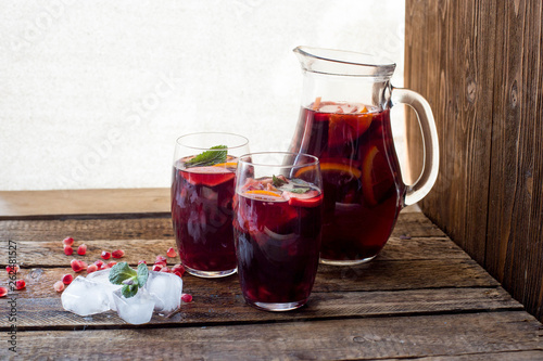 Refreshing homemade lemonade with ice, pomegranate, orange and mint. on a wooden table.
