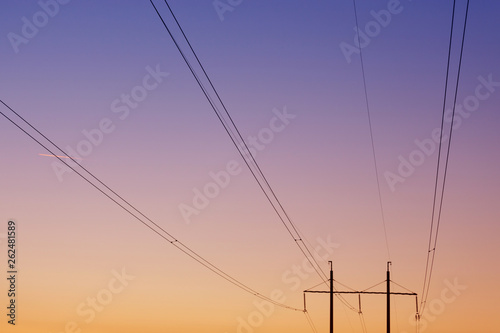 electrical wires against the dawn sky, in the background two pillars, focusing on the wires, concept