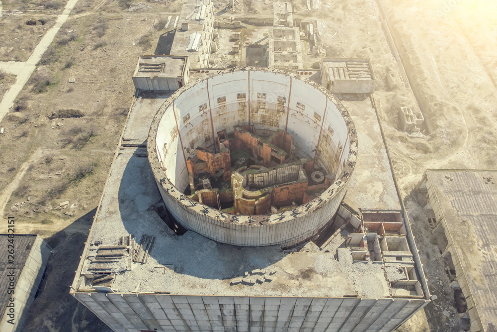 Aerial view from drone of abandoned and ruined Nuclear Power Plant or station, round tower of atomic reactor, large industrial demolished building