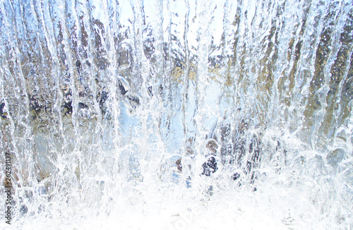 Transparent blue white water pours from above. View through the water wall of the waterfall for the background.