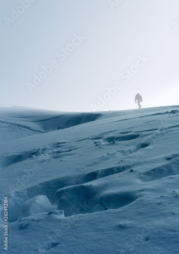 a lonely man on a snowy hill in the winter during a strong wind goes over the spine wrapped in warm clothes