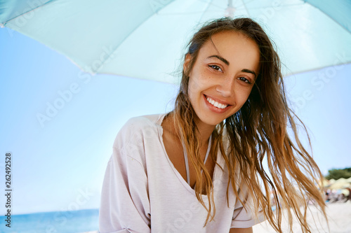 Beautiful sexy happy woman having fun on beach at resort. Young smiling woman in a white shirt at the beach with sea background. Model is relaxing lying down on white sand tropical getaway. Summer