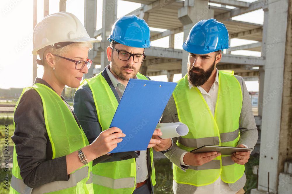 Small group of architects and civil engineers meeting on a construction site. Discussing future plans and looking at project documentation Small group of architects and civil engineers meeting on a construction site. Discussing future plans and looking at project documentation