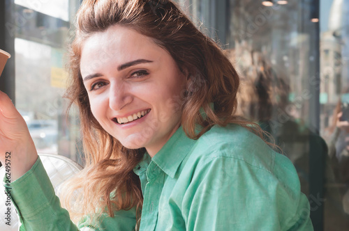 portrait of beautiful woman with long hair looking at camera and smiling near wondow in coffee shop photo