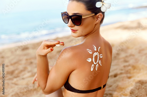 Woman Applying Sun Cream  on Tanned  Shoulder In Form Of The Sun. Sun Protection.Sun Cream. Skin and Body Care. Girl Using Sunscreen to Skin. Female Holding Suntan Lotion and Moisturizing Sunblock.