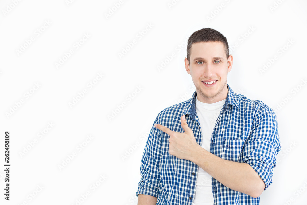 A stylish unshaven man in a shirt points to a copy of the space on a white wall, as something nice shows, has a smiling look, advertises a product. Look here! People, advertising, emotion concept A stylish unshaven man in a shirt points to a copy of the space on a white wall, as something nice shows, has a smiling look, advertises a product. Look here! People, advertising, emotion concept