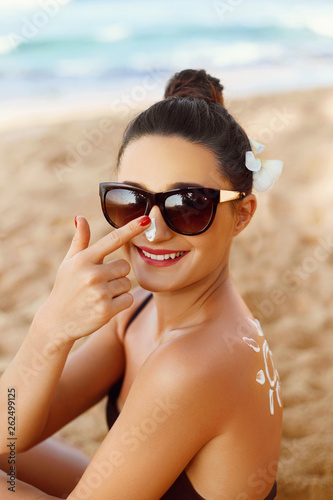 Suntan Lotion. Sexy Young Woman in Bikini  Applying Sunscreen Solar Cream.Sun Protection. Sun Cream. Skin and Body Care.Girl Holding Moisturizing Sunblock. Sun shape on the shoulder. Skin Protection