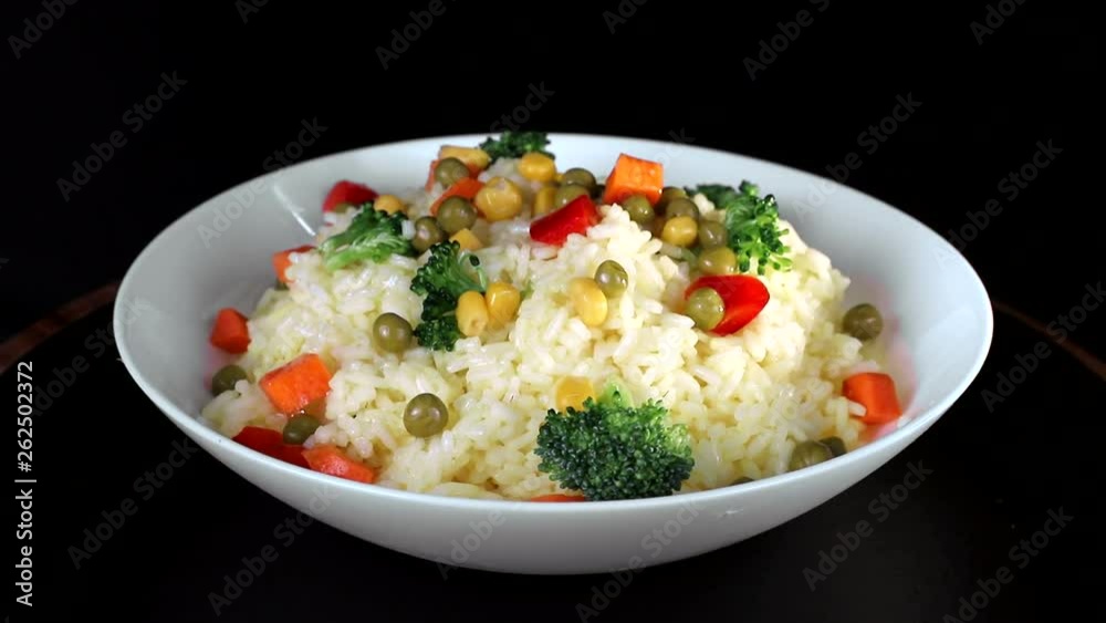 Rice with pieces of vegetables, greens and red pepper on a white plate rotates on a black background Rice with pieces of vegetables, greens and red pepper on a white plate rotates on a black background