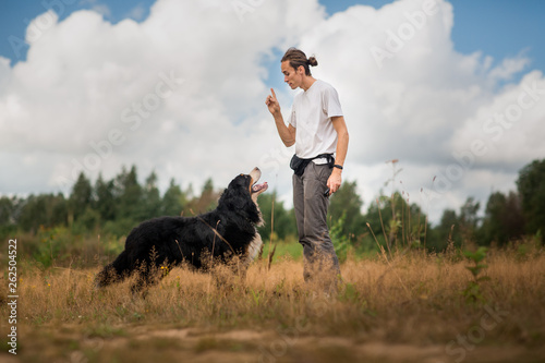 young man walking with Bernese Mountain Dog on the summer field © Alexandr