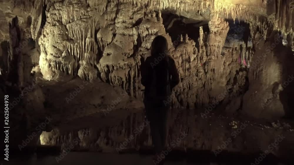tourist girl stands alone on the concrete bank of a small mountain river in a stone cave