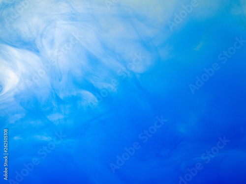 Drop of blue acrylic ink in water, close up view. Abstract background. Acrylic clouds swirling in liquid. Waves of paint in water, abstract pattern. Ink dissolving into liquid. Blurred background