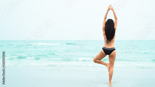 Asian model in bikini having yoga outdoor by blue sea