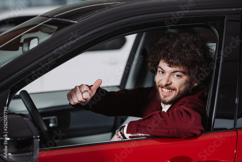 cheerful curly man sitting in car and showing thumb up
