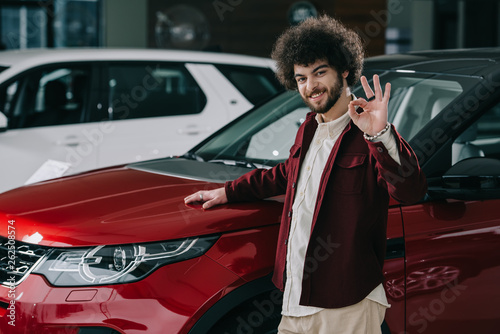 cheerful curly man showing k sign while standing near red car © LIGHTFIELD STUDIOS