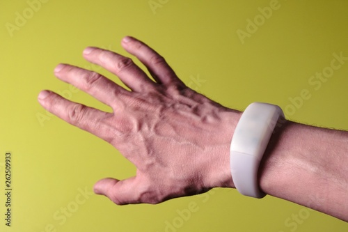 White bracelet like a smart watch or pixmob remote control on a man's hand with fingers spread. Green background. Modern gadget. Device for the show. Shallow depth of field. Selective focus. photo