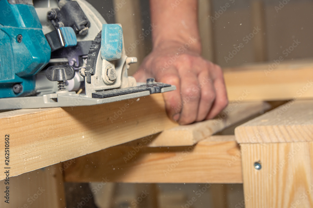 closeup man works with handheld battery saw on wooden surface