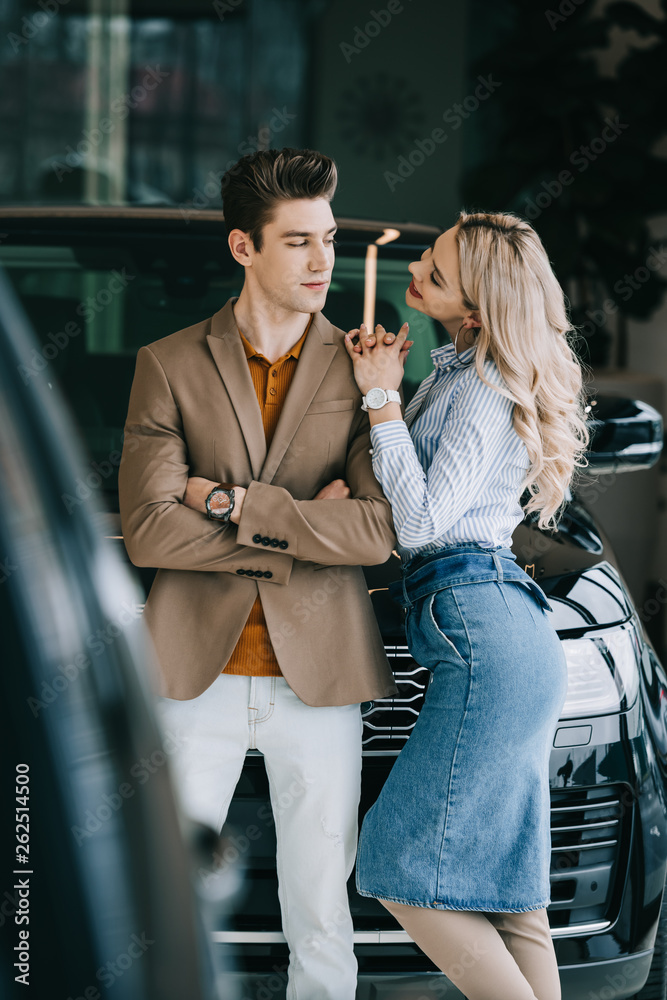 Fototapeta premium cheerful blonde girl looking at handsome man standing with crossed arms