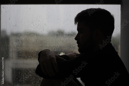 silhouette of a man sitting in the window with rain in mood of sadness and depression