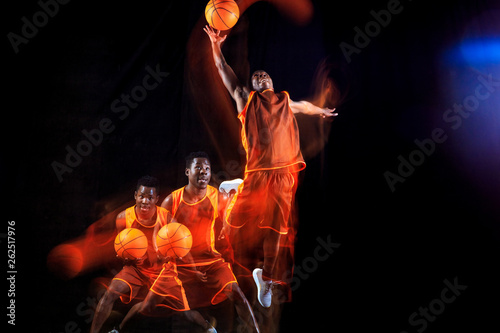 Higher than sky. African-american young basketball player of red team in action and neon lights over dark studio background. Concept of sport, movement, energy and dynamic, healthy lifestyle.