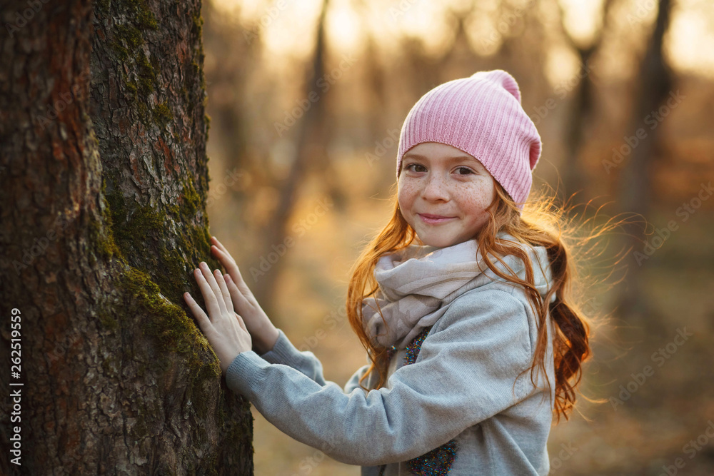Portrait of a pretty smiling girl with red hair and freckles near a tree. Spring or autumn park or forest. Sun rays. Concept of unity with nature Portrait of a pretty smiling girl with red hair and freckles near a tree. Spring or autumn park or forest. Sun rays. Concept of unity with nature