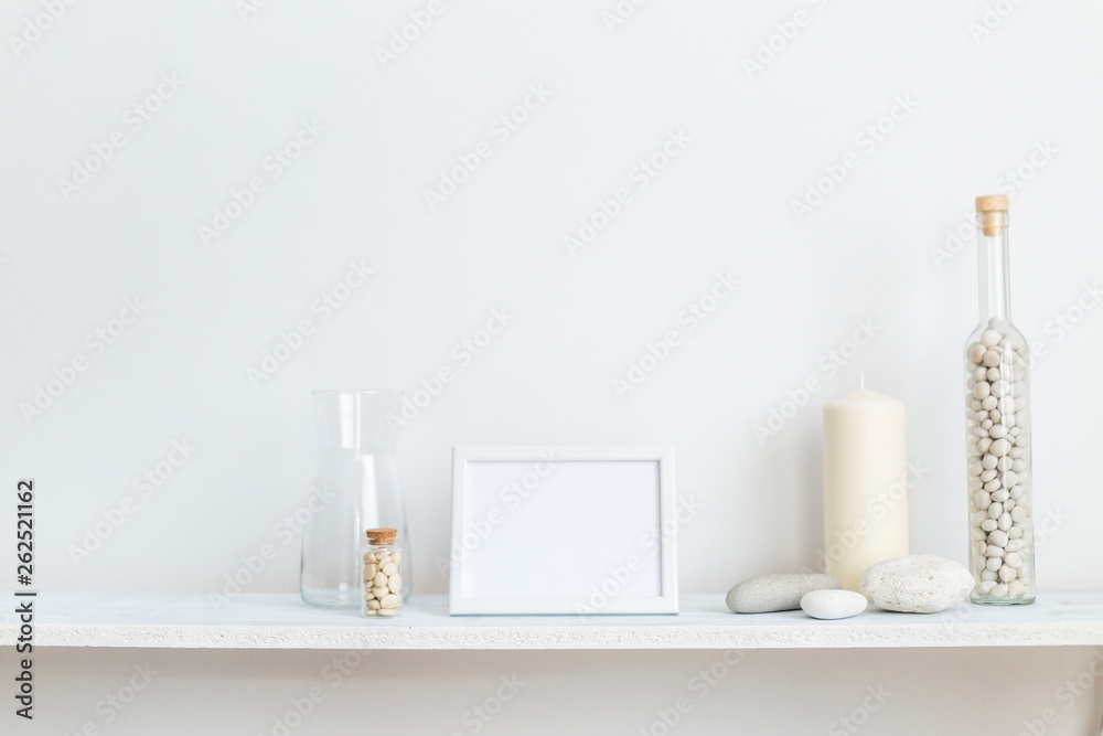 Shelf against white wall with decorative candle, glass and rocks.