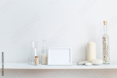 Shelf against white wall with decorative candle, glass and rocks. © MexChriss