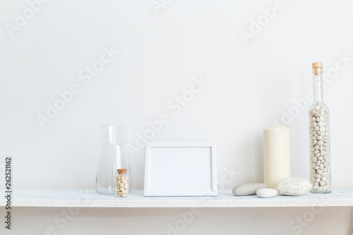Shelf against white wall with decorative candle  glass and rocks.