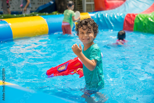 Cute boy playing in the swimming pool with water gun. Summer time. 