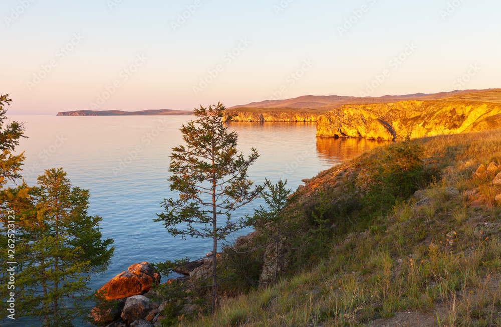 Baikal Lake. Coast of Olkhon Island. Summer sunset colored coastal cliffs in golden color. Beautiful landscape. Natural background