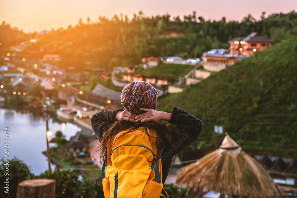 Young woman with backpack enjoying sunset on peak of  mountain. Tourists standing in a tea plantation watching the beautiful mountain sunshine at Ban Rak Thai village.