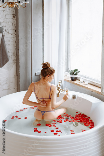 Beautiful girl with long curly hair in sexy underwear posing on bathroom background. A woman takes a big round bath with rose petals.