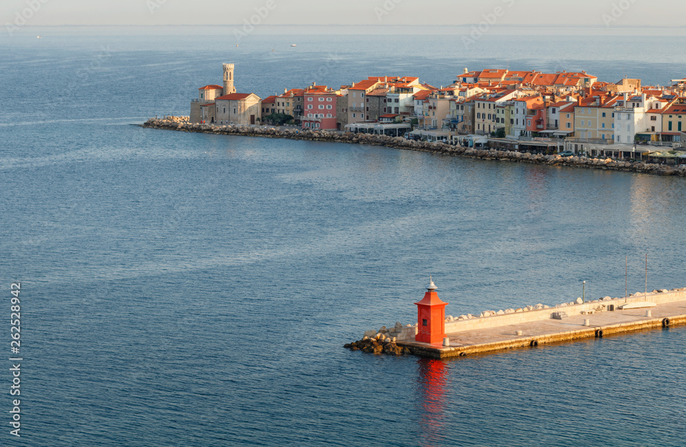 Skyline of Piran port and colorful houses during sunrise with old red lighthouse, Slovenia