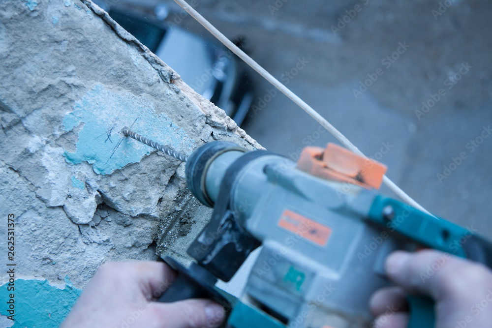 Repair and construction working indoors. Grunge background rubble and stones. Man's hands in gloves with a drill make a hole in the concrete. Surface preparation for work. Repair and construction working indoors. Grunge background rubble and stones. Man's hands in gloves with a drill make a hole in the concrete. Surface preparation for work.