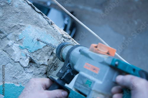 Repair and construction working indoors. Grunge background rubble and stones. Man's hands in gloves with a drill make a hole in the concrete. Surface preparation for work.