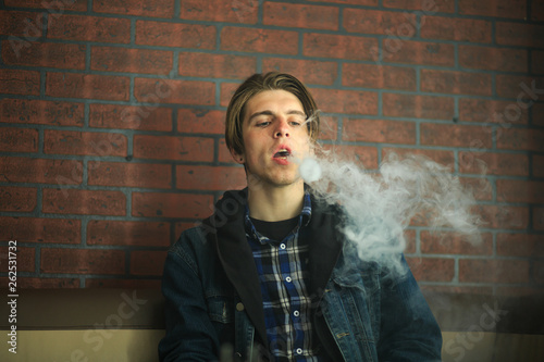Vape teenager. Portrait of young handsome guy smoking an electronic cigarette in the bar. Bad habit that is harmful to health. Vaping activity.